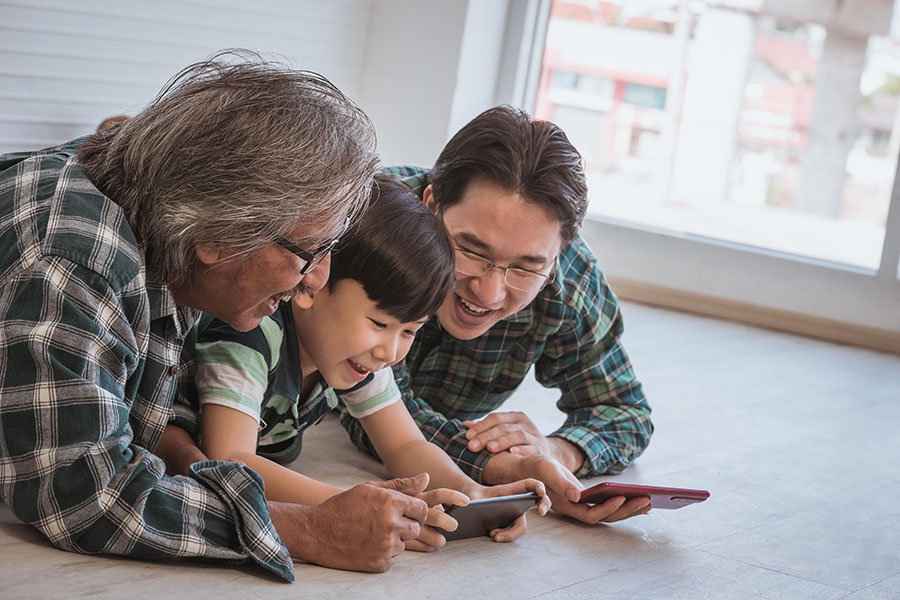 Client Portal - Smiling Father And Son Laying On The Floor Looking At Their Phone With Grandfather